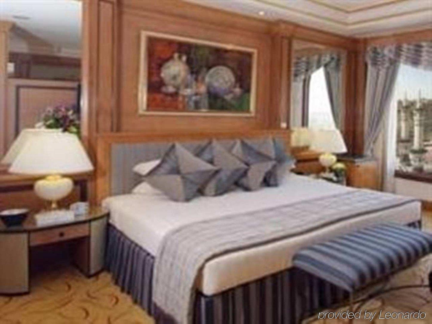 Makkah Hotel La Meca Exterior foto The image shows a luxurious hotel room. It features a large bed with several decorative pillows arranged on it. The bed has an elegant bedspread that goes with the room's overall decor. To the side, there are two bedside tables with lamps and a decor